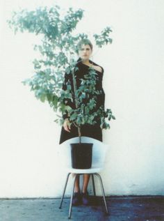 a woman sitting on a chair next to a potted plant in front of a white wall