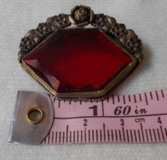 "For your consideration we have a lovely lapel pin/brooch from the Victorian era. This pin is stunning in detail and color, done with bright red glass stone and bordered on the top by a floral design of brass. We believe this pin was upcylced from a possible shoe buckle. Measuring approximately 1.5\" long and 1.25\" tall, this is a great accessory for any dapper gent or well turned out woman. Shipping policies: If you choose to pay via Paypal, you must either be a verified buyer, or provide a co Vintage Red Lapel Pin For Gift, Vintage Red Lapel Pin As Gift, Red Vintage Lapel Pin For Gift, Red Vintage Lapel Pin As Gift, Vintage Red Brooches For Formal Occasions, Antique Red Brooch As Gift, Antique Red Brooches As A Gift, Antique Red Brooches For Gift, Antique Red Brooches As Gift