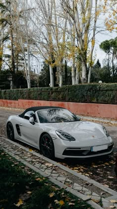 a white sports car parked on the side of the road in front of some trees