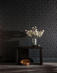 a vase filled with flowers sitting on top of a wooden table next to a wall