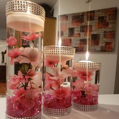 three vases filled with pink flowers and lit candles on a table in front of a mirror