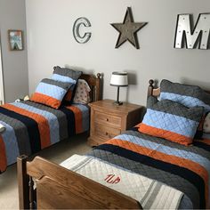 two beds in a bedroom with blue, orange and gray bedding on the covers