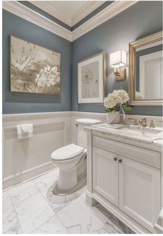 a white toilet sitting next to a sink in a bathroom under two framed pictures on the wall