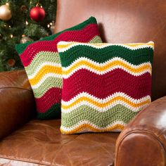 two crocheted pillows sitting on top of a brown leather chair next to a christmas tree