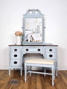 a blue vanity with a mirror and stool in front of it on a hard wood floor