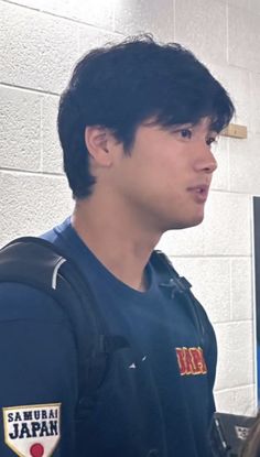 a young man wearing a backpack standing in front of a computer screen and looking off to the side