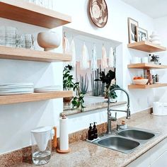 a kitchen with white walls and open shelving above the sink is filled with dishes