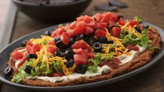 a pizza topped with lettuce, tomatoes and black olives on a plate