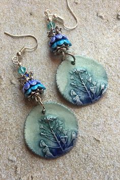 two earrings with blue flowers and leaves on them are sitting on the ground next to each other