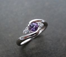 a ring with three diamonds and a purple stone in the center on a black surface