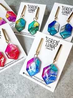 These irregular hexagonal dangle earrings showcase alcohol ink art, personally hand-drawn by me. They feature a vibrant mix of colours, accented with golden ink and a touch of glitter for a dazzling effect. The hexagonal pendants are paired with stainless steel rectangular bars, creating a striking contrast with their simple, clean lines. As wearable art and completely handmade, each piece is truly unique. Earrings are backed with in gold plated 304 stainless steel and butterfly back. Handmade i Alcohol Ink Jewelry, Earring Ideas, Alcohol Ink Art, Jewellery Handmade, Jewelry Card, Ink Art, Unique Earrings, Resin Jewelry, Alcohol Ink