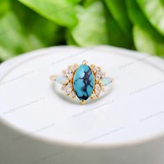 a ring with blue stones on it sitting on top of a white table next to green leaves