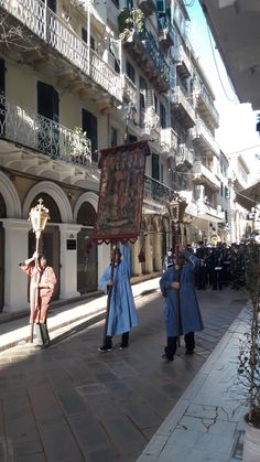 two men in blue robes are walking down the street with an easel on their back