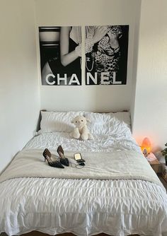 a white bed with two pairs of high heel shoes on it and a chanel poster above the bed