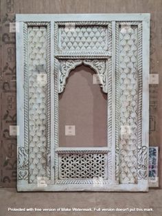 an ornate white window frame with intricate carvings on the outside and inside, in front of a wallpapered background