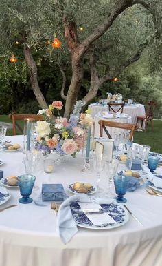 an outdoor table set up with blue and white plates, napkins and flowers on it