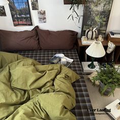 an unmade bed in a room with pictures on the wall above it and plants