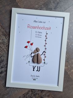 a white frame holding two rocks with flowers on them and the words rosenhochzeit written in german