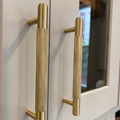 two gold handles on the front door of a white cabinet with a mirror behind it