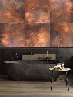 a bath tub sitting next to a wooden table in a room with large tiles on the wall