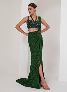 This elegant Emerald Green Pre-Draped Saree is meticulously crafted from a luxurious blend of crepe and platinoir crepe, offering a rich texture and impeccable drape. The green saree merges traditional charm with modern flair, featuring all-over metallic detailing that adds a subtle, luxurious sheen. Paired with a sleeveless halter neck blouse, intricately adorned with dangling halo nalki embellishments, making it both chic and sophisticated. A hand-embellished belt cinches the waist, adding a contemporary edge to this timeless look. Perfect for cocktails, Sangeet nights, or evening parties, this outfit ensures you stand out with grace, elegance, and style. Composition : Blouse - Crepe blend, Saree - Platinoir Crepe Care: Dry Clean Only and Vacuum Storage This product can be customized for Halter Neck Blouse, Halter Neck Blouses, Draped Saree, Embellished Belt, Vacuum Storage, Drape Saree, Indian Wedding Wear, Green Saree, Wedding Wear