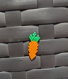 an orange and green beaded carrot sitting on top of a woven piece of wood