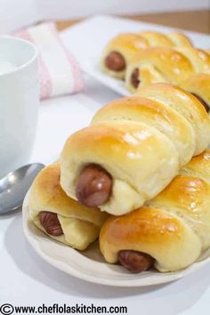 hotdogs wrapped in bread on a plate with a cup of coffee and spoon