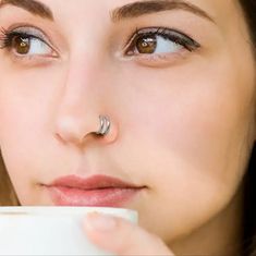 a close up of a woman with a nose ring on her nose drinking from a cup