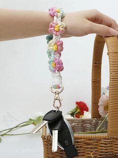 a hand holding a key chain attached to a basket with flowers in the back ground