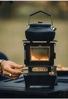 a black stove sitting on top of a table next to a person's hand