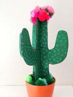 a green cactus with pink flowers sitting in a pot on top of a white table