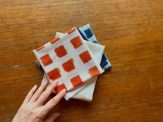 a person's hand on top of three napkins sitting on a wooden table