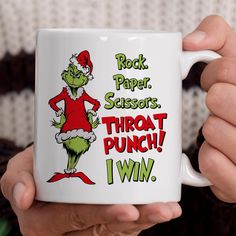 a person holding a coffee mug with the grinch on it's side, reading rock paper scissors throats throat punch i win