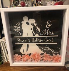 a wedding cake topper in a white frame with pink flowers on the bottom and a bride and groom's silhouette