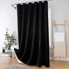 a black shower curtain in a bathroom with wood flooring and white walls, along with a rug on the floor