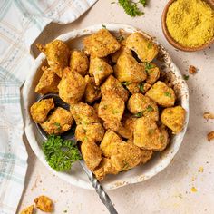 a white bowl filled with fried food next to a spoon and some yellow powder on the side