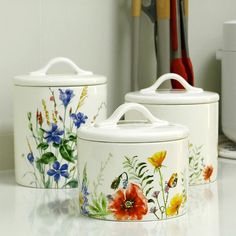 three white canisters with colorful flowers painted on them