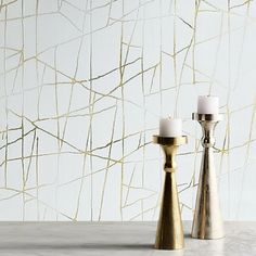 two candles are sitting next to each other in front of a wall with gold paint