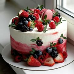 a cake with berries and strawberries on top is sitting by a window sill