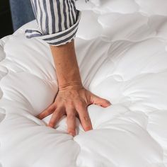 a person's hand on top of an unmade bed with white comforter