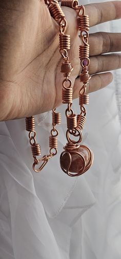 a woman's hand holding onto a bracelet made out of copper wire and charms