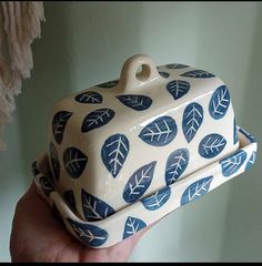 a hand holding a ceramic container with blue leaves on it