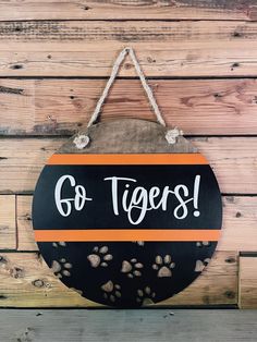 a black and orange sign that says go tigers with paw prints hanging from the side of a wooden wall