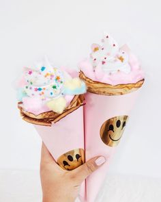 two ice cream cones with smiley faces and sprinkles on them are being held by someone's hand