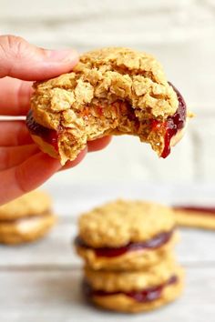 a hand holding a peanut butter and jelly oatmeal cookie over three cookies