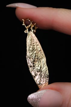 a close up of a person's hand holding a gold necklace with a leaf on it