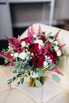 a vase filled with red and white flowers sitting on top of a table next to a chair