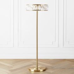 a gold floor lamp on a wooden floor in front of a white wall and wood floors