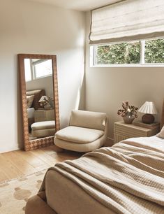 a bedroom with a bed, chair and large mirror in front of the window on the wall