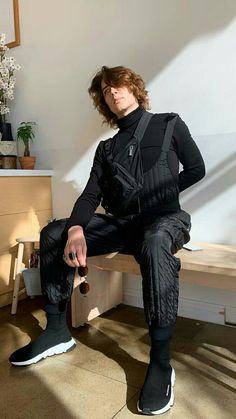 a man sitting on top of a wooden bench next to a white vase filled with flowers